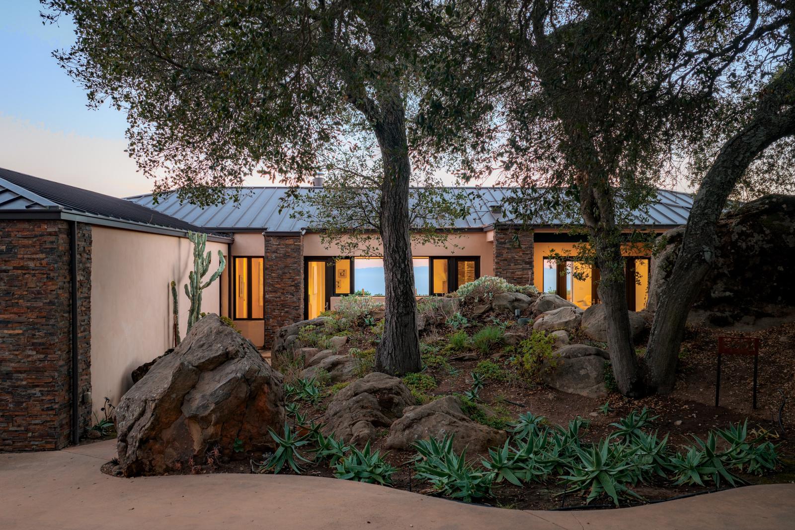 The house at dusk among live oaks and sandstone boulders